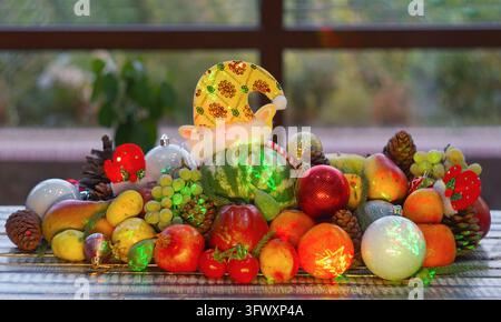 A wide horizontal eye-level shot of a festive Christmas fruit display on a wooden table, featuring a small green striped watermelon in a sparkling yel Stock Photo