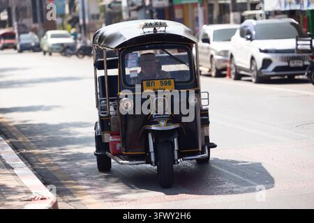 Chiang Mai, Thailand - January 17, 2026: A black three-wheeled tuk-tuk taxi with Thai script and number 596 drives down a sunlit urban street lined… Stock Photo
