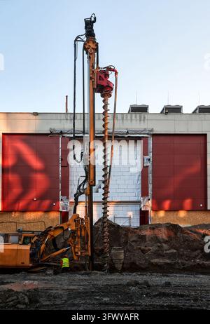 Foundation drilling and ground engineering beside a building at an urban construction site. A rotary drilling rig with a large auger Stock Photo
