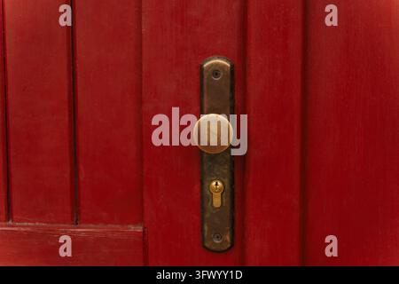Close up of a circular antique brass knob and keyhole on a vibrant red vertical wooden door, showcasing rustic textures and classic architecture Stock Photo