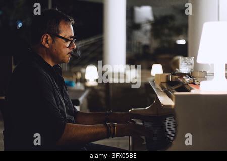 A male middle-aged white Caucasian pianist playing easy jazz in a piano lounge for a party, smoking a cigar Stock Photo