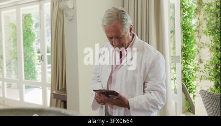 Portrait of caucasian senior male doctor smiling while using digital tablet at home Stock Photo
