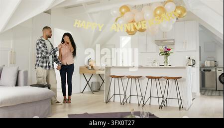 Happy black man and multiracial woman walking into room, embracing, sitting on blanket, having anniv Stock Photo