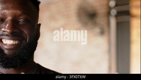 African American man standing and smiling in loft with brick wall and metal beam, copy space Stock Photo
