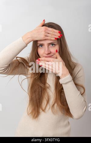 Woman standing against white background, framing her happy smiling face with hands into a square shape, looking at the camera with red nails and light Stock Photo