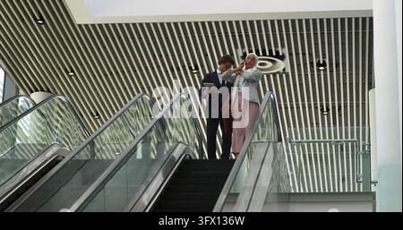 Caucasian man and young woman discuss work on an escalator Stock Photo