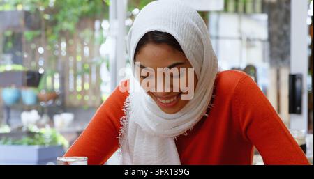 A hijab-clad woman enjoys a serene moment in a sunny cafe. Stock Photo