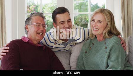Image portrait of happy caucasian husband and wife sitting on couch with senior father smiling Stock Photo
