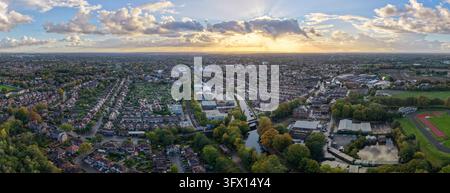 Wide drone panorama of Stretford under a golden sunset, showing Bridgewater Canal, a tram line, allotments, an athletics track and rows of terraced ho Stock Photo