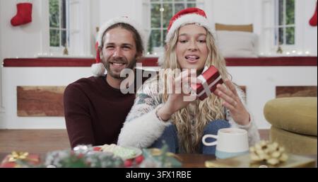 Happy diverse couple wearing santa hats having christmas image call at home Stock Photo
