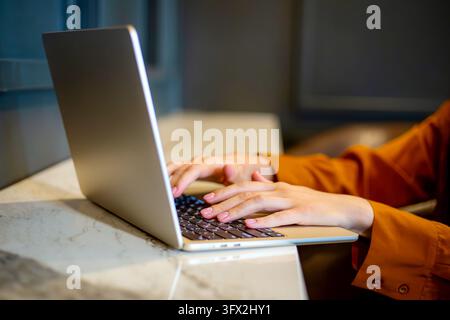 Female hands typing on a laptop in a modern workspace, showing a woman engaged in remote work, digital tasks and contemporary technology use in a Stock Photo
