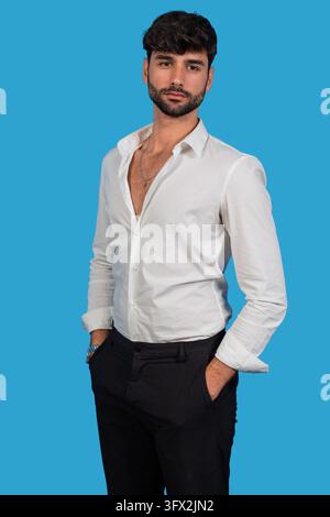 Bearded man in an open white shirt posing confidently against a bright blue studio background Stock Photo