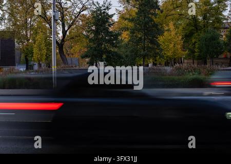 Passing passenger car with blurred bodywork and illuminated rear lamps on a marked city road, illustrating urban vehicle traffic and everyday road tra Stock Photo