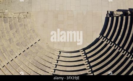 Ancient Kourion theater curved stone seating and orchestra floor, with strong sunlight casting dramatic shadows on the steps of the historical Roman amphitheater in Limassol. Aerial view drone shot Stock Photo
