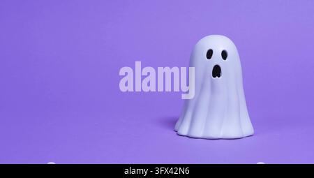Front view of a white ceramic ghost with a black face against a purple background Stock Photo