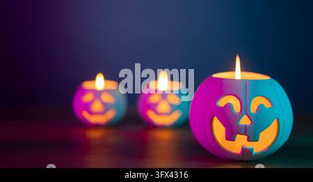 Front view of white pumpkin-shaped ceramic pot containing a lit candle featuring yellow face illuminated by purple and cyan light in the foreground se Stock Photo