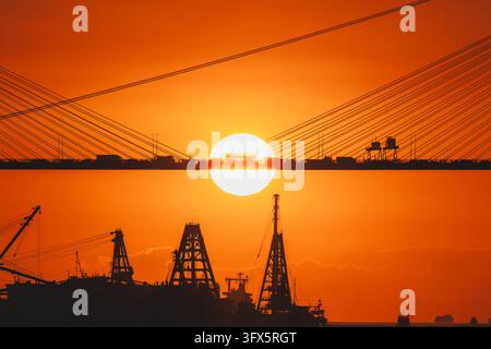 A striking telephoto sunset photograph capturing a Hong Kong public bus silhouetted against a giant setting sun on the Ting Kau Bridge, framed by harb Stock Photo