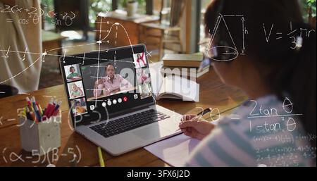 Studying girl wearing striped top writing in notebook at home table, with laptop showing class Stock Photo