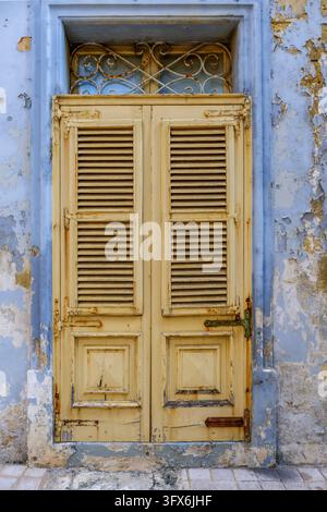 Front View of Vintage Yellow Louvered Wooden Front Door Set in Peeling Light Blue Painted Architrave Wall, Malta Stock Photo