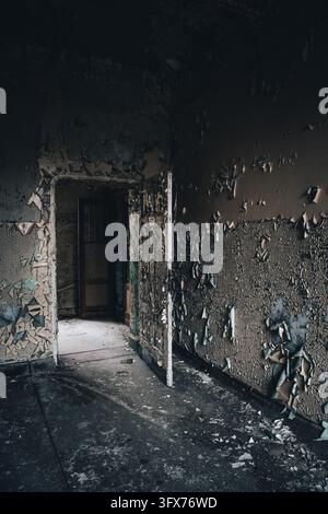 A decaying corridor in an abandoned building in Berlin, Germany, has an open doorway, peeling walls and rubble scattered across the dark floor. Stock Photo