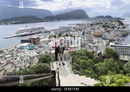 Young couple enjoying the panoramic view of Alesund city from Aksla viewpoint in Norway. Tourists standing on a glass observation deck looking at Ales Stock Photo