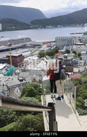 Young couple enjoying the panoramic view of Alesund city from Aksla viewpoint in Norway. Tourists standing on a glass observation deck looking at Ales Stock Photo