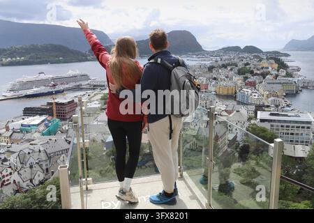 Young couple enjoying the panoramic view of Alesund city from Aksla viewpoint in Norway. Tourists standing on a glass observation deck looking at Ales Stock Photo
