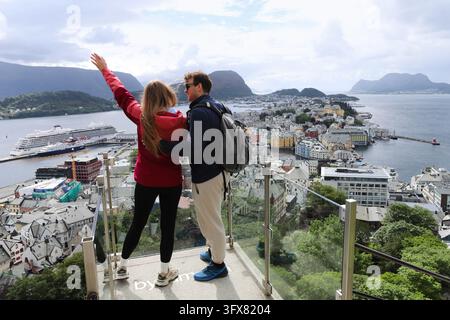 Young couple enjoying the panoramic view of Alesund city from Aksla viewpoint in Norway. Tourists standing on a glass observation deck looking at Ales Stock Photo