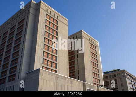 Brooklyn, NY – Sep 4, 2023: Low-angle view of two MDC Brooklyn towers with narrow windows rising above a concrete wall against a clear blue sky. Stock Photo