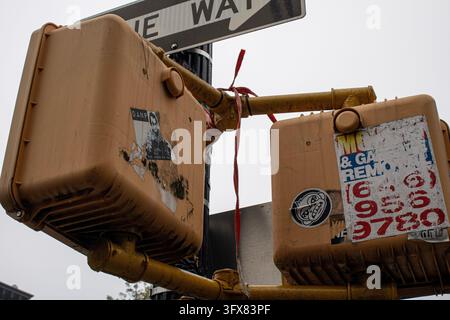 New York City, USA – October 6, 2023: Two yellow pedestrian signal boxes covered in stickers and advertising flyers below a one-way sign. Stock Photo