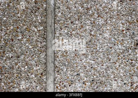 Exposed aggregate concrete pavement with small multicolored pebbles and a central concrete strip, close up weathered outdoor surface in Thailand. Stock Photo