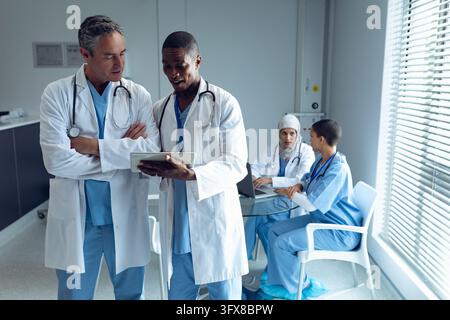 Front view of diverse male doctors discussing over digital tablet and female doctors using laptop in hospital Stock Photo