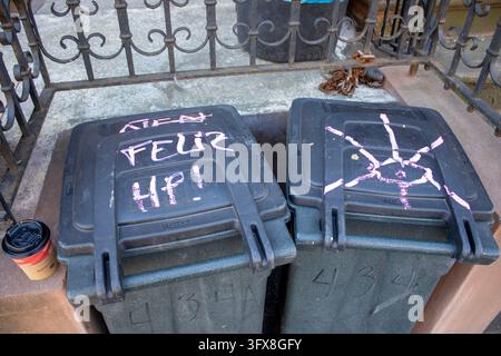 New York City, USA – February 7, 2024: Two grey trash cans with chalk writing and an eye drawing on their lids beside a disposable coffee cup. Stock Photo