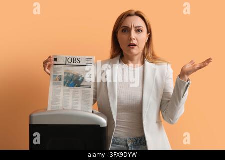 Unemployment and job loss concept, woman holding a newspaper with jobs headline near a paper shredder with a frustrated and confused facial expression Stock Photo