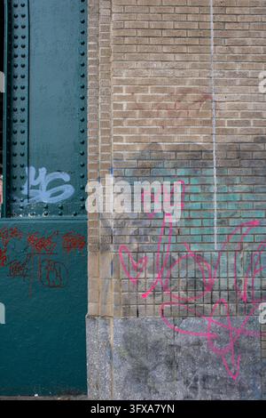 New York City, USA – February 12, 2024: Faded pink and blue graffiti on a brick wall beside a riveted green steel column. Stock Photo