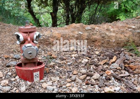 BARCELONA, SPAIN - 2025-04-15: A red fire hydrant with a visible AENOR 'Producto Certificado' (Certified Product) label stands in a rocky, wooded area Stock Photo