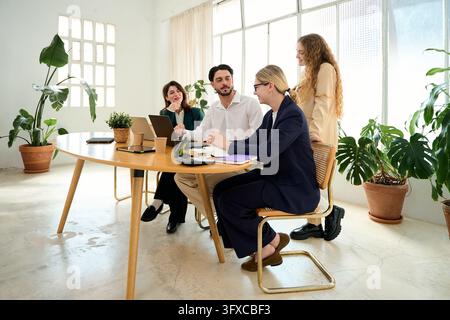 Diverse business professionals collaborating and discussing work around a modern table during an office meeting, fostering teamwork and planning Stock Photo