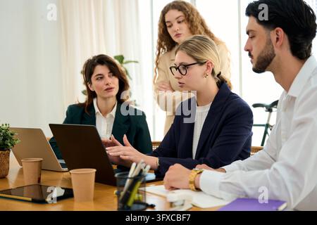 Diverse business professionals discussing project data around a conference table in a modern office, engaged in a team meeting Stock Photo