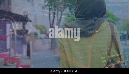 Walking woman in headscarf and mustard coat carrying shoulder bag along sidewalk amid market charts. Urban, street, scarf, satchel, silhouette, moody, Stock Photo