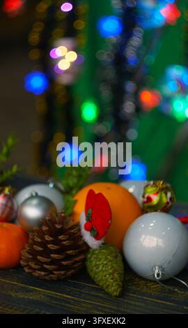 A vertical close-up photograph of a festive holiday arrangement featuring fresh oranges, tangerines, brown and green pine cones, a tiny Santa hat deco Stock Photo