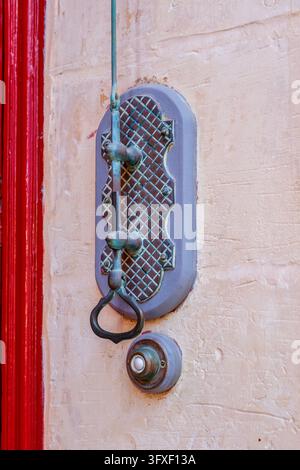 Antique Vertical Door Pull Rod with Decorative Grid Backplate and Electric Bell Button Mounted on Stucco Wall Stock Photo