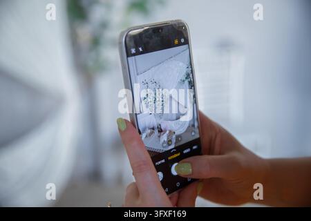 A woman taking a photo of a beautifully decorated wedding photo zone using her smartphone screen. Modern mobile photography capturing elegant festive Stock Photo