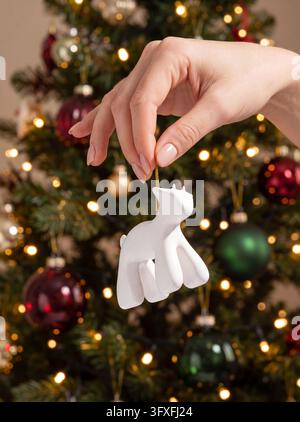 Woman hangs a white animal ornament on a Christmas tree Stock Photo