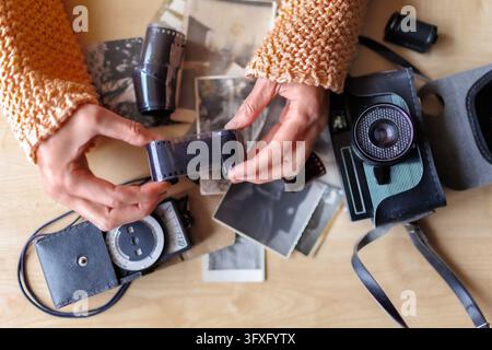 Hands holding developed photographic film among vintage camera, light meter, old black and white photographs on wooden table. Analog photography Stock Photo