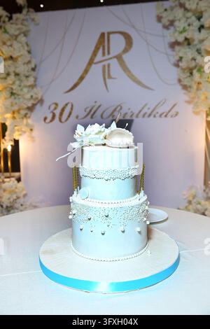 Elegant two-tier white celebration cake decorated with pearls, delicate flowers, and an open seashell topper. The luxurious dessert is displayed again Stock Photo