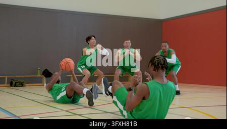 Diverse teammates starting core drill in gym, passing basketball doing sit-ups squatting clapping. Athleticism, teamwork, motivation, active, fitness, Stock Photo