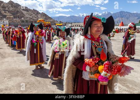 Women in traditional headdresses carrying flower bouquets in a procession on a festival ground, Ladakh, Leh, India Stock Photo
