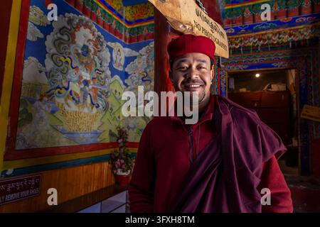 Portrait of a smiling monk in red robe and cap standing at the entrance of Hemis monastery, Ladakh, Hemis, India Stock Photo