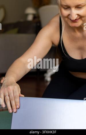 Close up of a smiling middle aged woman hands adjusting a laptop screen before starting an online yoga practice on a mat. Concept of e-learning, digit Stock Photo