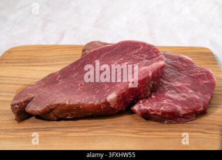 Two Slices of raw beef steak on a wooden cutting board Stock Photo